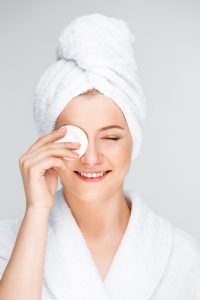 Woman in bathrobe bathing her eye after brow tattoo.