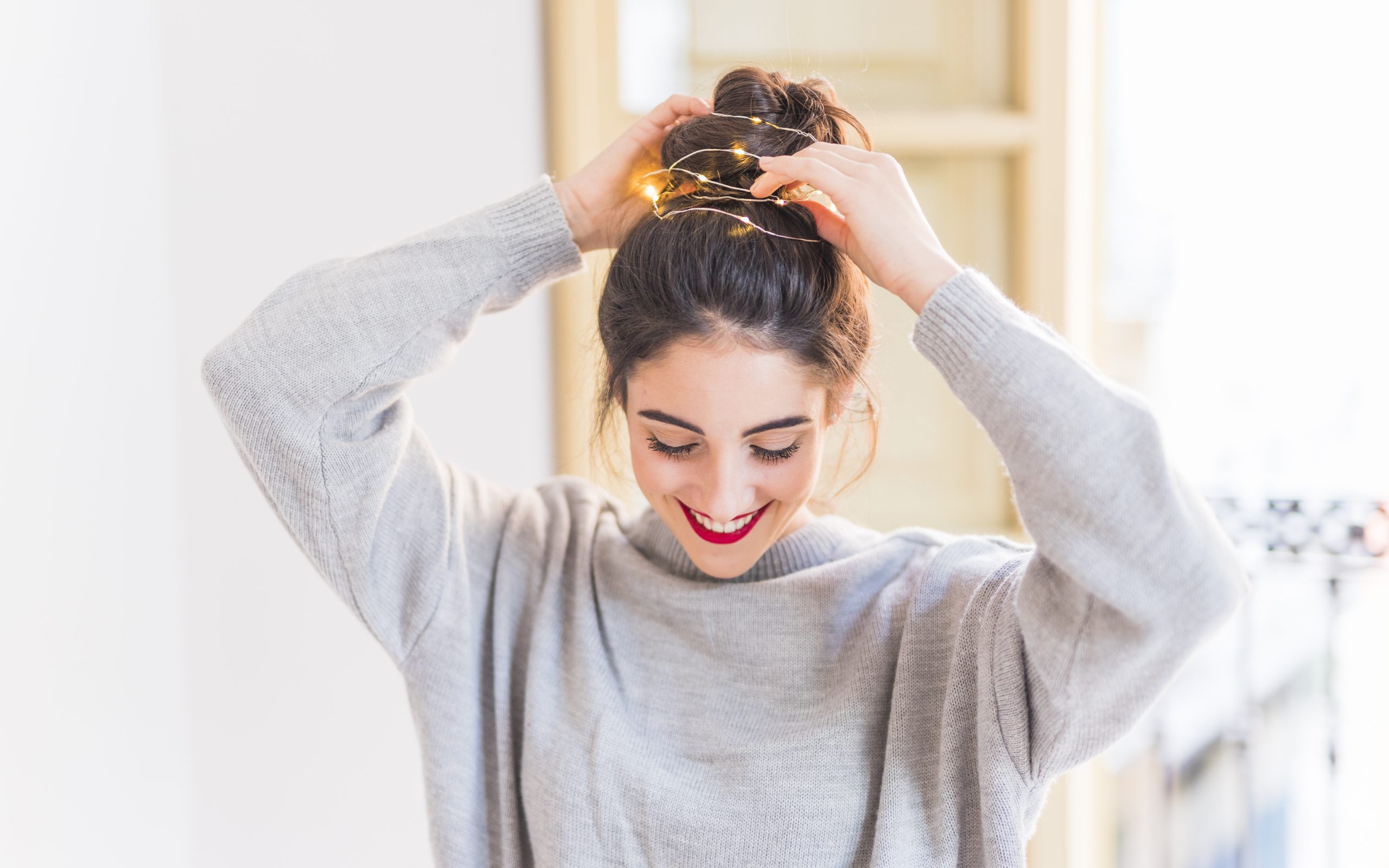 Young woman wrapping Christmas lights around her head. She is looking down showcasing Cara's Semi-permanent Eyeliner Tattoos.