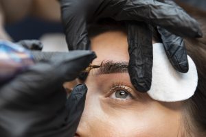 A technician using a tool to apply pigment during a semi-permanent Ombre Brows procedure.